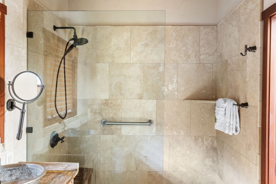 Glass-enclosed shower with rainfall showerhead and tile inlay—modern function meets tropical style.