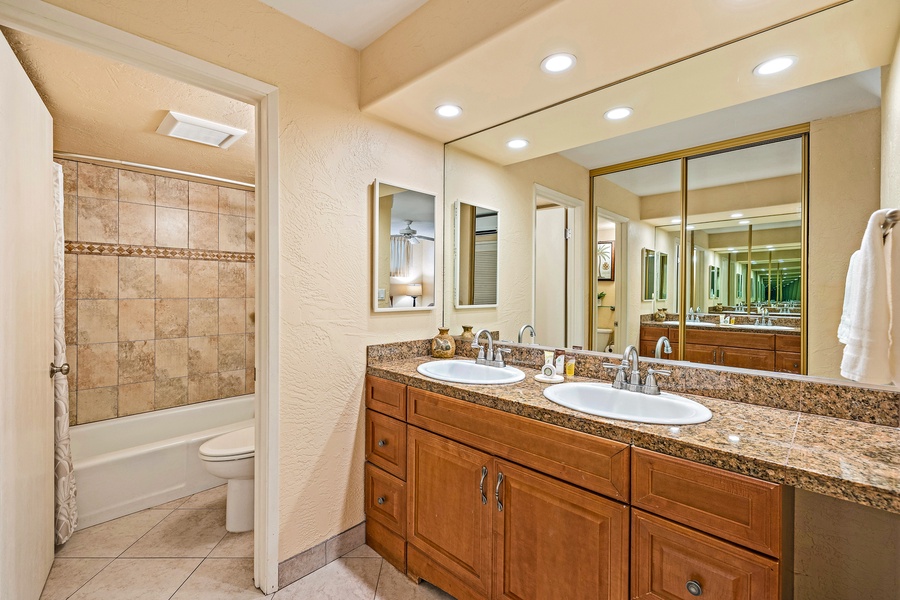 The bathroom features a double vanity and well-lit mirrors, along with a shower and tub combination for a relaxing soak.