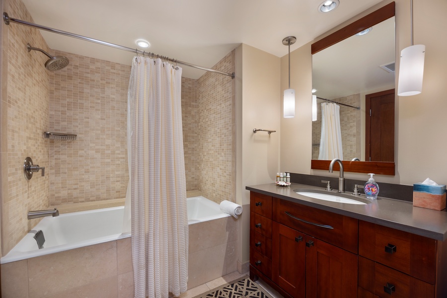 Unwind in your spa-like bathroom featuring elegant mosaic tiles, a deep soaking tub, and warm wood vanity with modern pendant lighting.