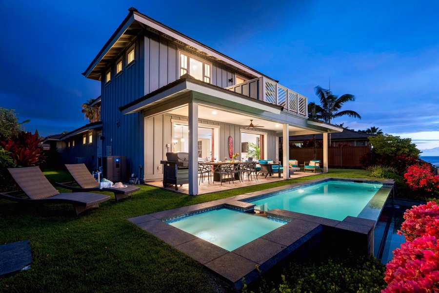 Elegant two-story home illuminated at twilight, featuring a spacious pool area and a cozy outdoor dining space.