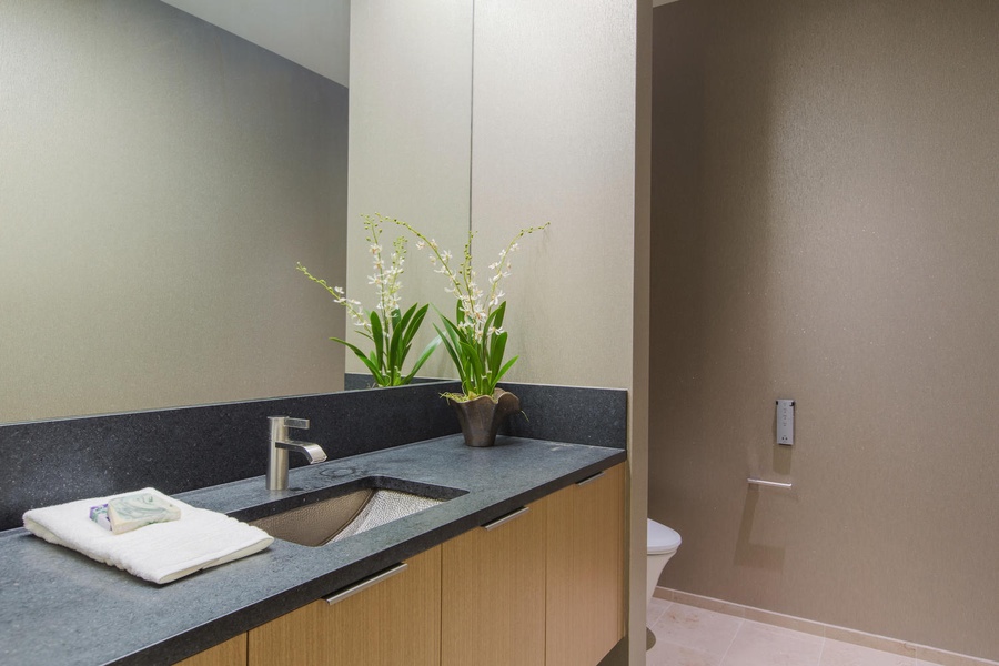 Step into your stylish bathroom featuring a sleek granite vanity, modern fixtures, and thoughtful touches like fresh orchids that make your stay feel special.