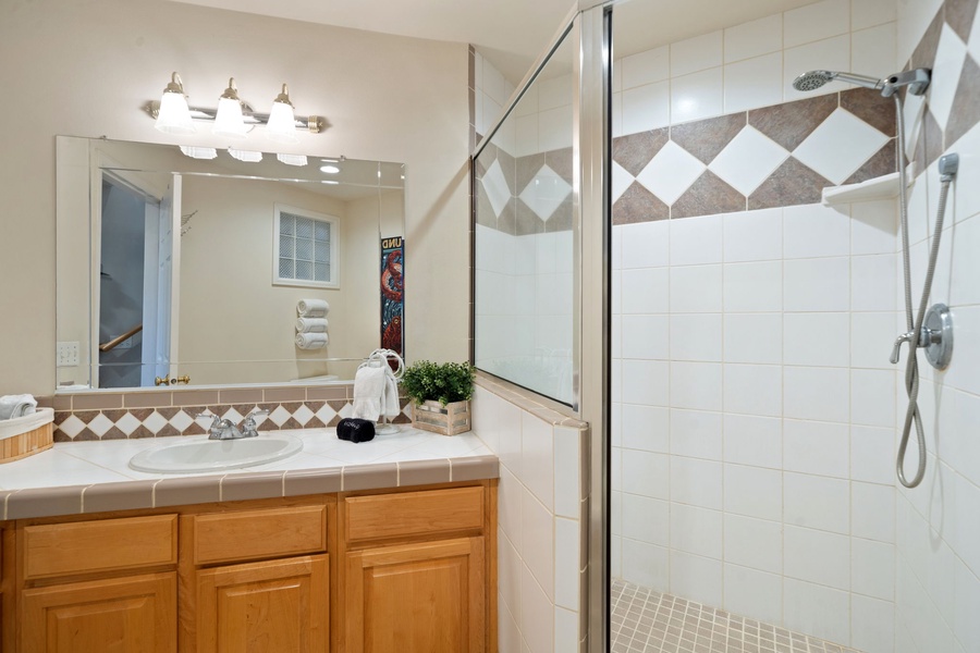Refresh in your private bathroom featuring a glass-enclosed shower with decorative tilework and a vanity with warm wood cabinetry.