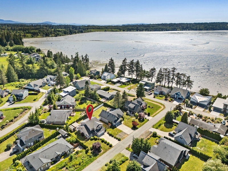 Aerial view of a waterfront community with homes nestled along lush green shoreline and serene tidal flats, perfect for peaceful getaways.